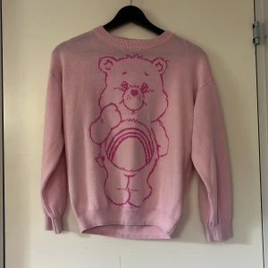 Rosa Care Bears stickad tröja H&M - Supergullig rosa stickad tröja från H&M x Care Bears med stor björn på framsidan. Text i rosa på ärmarna. Mjuk och skön. Rund hals och långa ärmar. Ytterst små fläckar på framsidan (se bild 4) och lite nopprig annars i bra skick!