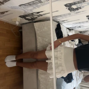 Vit volangkjol med struktur - Supersöt vit kortkjol med volanger och strukturerat tyg. Kjolen har en bred midja och flera lager volang som ger en fluffig och trendig look. Perfekt att styla med en crop top eller hoodie för en chill vibe.