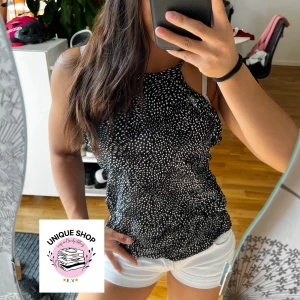 Svartvit prickig linnetopp - Snygg svart linnetopp med vita prickar och tunna axelband. Toppen har en rak, något lös passform och hög halsringning. Perfekt för varma dagar och enkel att matcha med shorts eller kjol. Lätt och luftig känsla.