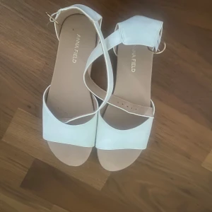 Vita sandaler från Anna Field - Snygga vita sandaler från Anna Field med bred rem över tårna och justerbar rem runt ankeln med guldfärgat spänne. Platt sula och öppen tå ger en clean och fräsch look, perfekt till sommarens outfits. Andvänt knappt 1 gång. Pris kan diskuteras.
