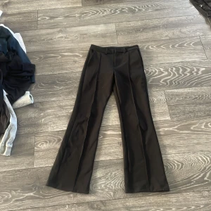 Svarta kostymbyxor från Kappahl - Svarta kostymbyxor från Kappahl med klassisk rak passform och pressveck framtill. Byxorna har hällor för bälte och sidfickor, perfekta för en clean och stilren look. Materialet känns mjukt och följsamt.