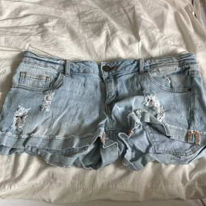 Ljusa jeansshorts - Snygga ljusblå jeansshorts från Review med slitna detaljer. Shortsen har orangea sömmar och låg midja. 