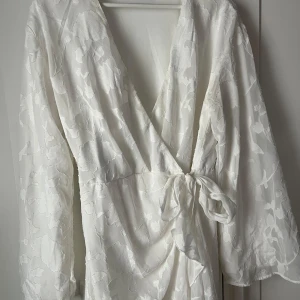 Vit omlottklänning från Gina Tricot - Superfin vit omlottklänning med blommigt mönster i tyget från Gina Tricot. Klänningen har långa, lite vida ärmar 