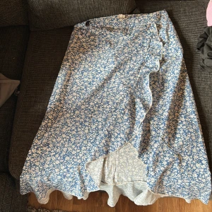 Blommig omlottkjol från SHEIN XS - Supersöt långkjol från SHEIN i blått med vitt blommönster. Kjolen har omlottmodell med volangkant längs nederdelen och är i ett lätt och skönt material. Perfekt för dig som gillar romantisk och somrig stil.