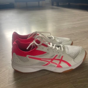 Vita och rosa sneakers från Asics - Snygga Asics sneakers i vitt och starkt rosa med meshdetaljer och klassisk logga på sidan. Skorna har snörning, platt sula och gummidetaljer för extra grepp. Skorna har använts få gånger och är i bra skick 