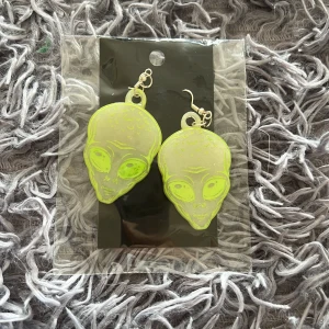 Neongröna alien örhängen - Coola örhängen i form av alienhuvuden i neongrönt. De är lätta och har krokar i silverfärg. Perfekta för dig som vill sticka ut med ett unikt och lekfullt smycke. Passar till dig som gillar udda accessoarer och vill ha något som syns.
