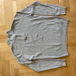 Grå ribbad tröja Hampton Republic - Säljer en grå ribbad tröja från Hampton Republic i storlek M. Tröjan har en hög krage med half zip-dragkedja och är långärmad. Perfekt för dig som gillar en clean och stilren look. Materialet är mjukt och stretchigt, vilket gör den riktigt skön att bära.