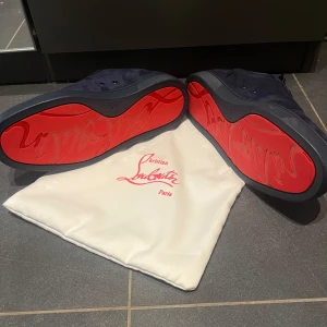 Mörkblå mocka sneakers från Louboutin - Snygga mörkblå sneakers i mocka från Christian Louboutin med ikoniska röda sulor. Skorna har rund tå, platt sula och klassisk snörning. Perfekt för dig som vill sticka ut med exklusiv design och lyxig känsla. Hör av er vid minsta lilla fundering. Priset går självklart ner vid snabbköp.
