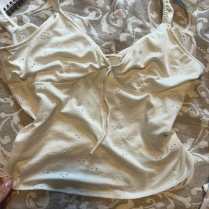 Vit linnetopp med broderade detaljer - Supersöt vit linnetopp med tunna axelband och broderade hålmönster. Toppen har en knytning bak och v ringad fram. Perfekt sommar topp. Den är S men skulle vilja säga att den är M ungefär. Om du har ganska stor överdel så vill jag påpeka att ”kuperna” på denna toppen inte är för dem ☺️