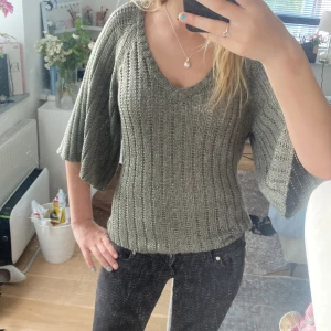 Olivgrön stickad tröja med v-ringning - Säljer en olivgrön stickad tröja med bred v-ringning och trekvartsärmar. Tröjan har ett ribbat mönster och är i en loose passform, perfekt för lager-på-lager. Skön och avslappnad stil som funkar året runt.