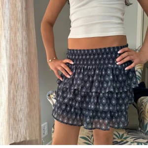 Volangkjol - Supersöt mörkblå kortkjol med volanger och droppformat mönster. Kjolen har en stretchig resår i midjan och flera lager volanger som ger en riktigt flowy känsla. Perfekt att styla med en enkel topp och sneakers. 170 barn, men passar även XS, S