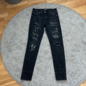Svarta skinny jeans från Amiri - Svarta skinny jeans från Amiri med slitna detaljer och trasiga partier framtill. Jeansen har en tight passform, klassisk femficksdesign och diskreta logodetaljer. Perfekta för dig som gillar en edgy och trendig look.