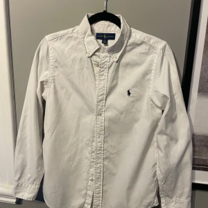 Vit skjorta från Ralph Lauren - Klassisk vit skjorta från Ralph Lauren. En stilren Shorta i bra skick. Obs! Det finns en liten fläck längst ner på armen som finns att de på bild 3