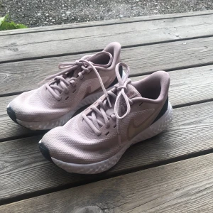 Nike sneakers i ljusrosa mesh - Nike sneakers i en snygg ljusrosa färg med mesh-ovandel och vit, vågformad sula. Skorna har snörning och diskret Nike-logga i rosa på sidan. Perfekta för dig som gillar sportig stil och vill ha bekväma skor till vardagen.