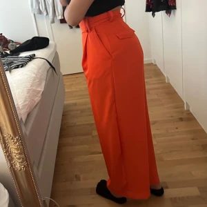 Orange vida kostymbyxor - Säljer ett par orangea kostymbyxor med hög midja och vida ben från Weekday. Byxorna har bälteshällor, fickor fram och en dekorativ ficka bak. De är i mycket bra skick, det märks att materialet är bra kvalité.