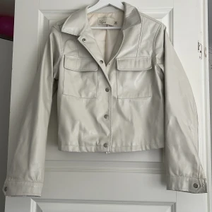 Vit skinnjacka från NLY Trend, stl 36 - Snygg vit glansig ”skinnjacka” från NLY Trend i storlek 36. Passar bra för mig som har strl S med en tjockare tröja under. 150kr+frakt. Inga tydliga defekter.