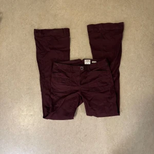 Vinröda bootcut byxor - SPARSAMT ANVÄNDA snygga vinröda byxor med bootcut passform och klassisk femficksdesign. Byxorna har normal midja och är tillverkade i ett mjukt bomullsmaterial med lite stretch för extra komfort. Perfekta för dig som vill ha en stilren men ändå avslappnad look.