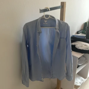 Ljusblå skjorta från ARKET  - Snygg ljusblå skjorta från ARKET med klassisk krage och bröstficka. Skjortan har långa ärmar och knäppning framtill. Perfekt för en clean och stilren look. Storlek 46 och passar någon som är 175 cm