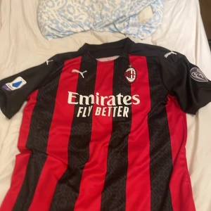 AC Milan matchtröja Puma röd/svart - AC Milan fotbollströja från Puma med klassiska röda och svarta ränder, klubbmärke på bröstet och sponsortryck. Kortärmad modell med svarta ärmar och vita Puma-loggor och Champions leuge merkä med. Perfekt för dig som älskar italiensk fotboll och vill bära klubbens färger. Äkta utan kvitto tyvärr i storlek Xl/L priset kan droppas vid snabb affär 