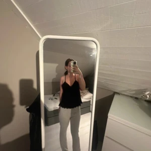 Svart linnetopp med tunna axelband - Säljer en svart linnetopp med tunna axelband och v-ringning. Toppen har en lös passform och vågig nederkant som ger en söt touch. Perfekt att styla med jeans eller kjol för en chill look.