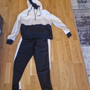 Svarta och vita mjukisset från Amisu - Snyggt svarta/vit mjukisset från Amisu med vita sidopaneler. Byxorna har elastisk midja i storlek s och är perfekta för chill eller träning. Matchar med hoodie i samma färgblock i storlek Xl för en clean och sportig look.