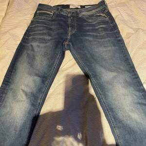 Blå Replay Grover Hyperflex jeans - Säljer ett par blå Replay Grover Hyperflex jeans med klassisk femficksdesign och snygga slitningar. Jeansen har raka ben, normal passform och är tillverkade i stretchigt denim för extra komfort. Bakfickorna har Replay-logga och coola sömdetaljer.