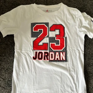 Jordan T-shirt  - Gör din streetwear-look komplett med denna klassiska vita Jordan T-shirt. Tillverkad i mjuk bomull med den ikoniska Jumpman-loggan tryckt framtill – enkel, stilren och alltid rätt. Perfekt till jeans, shorts eller under en hoodie.