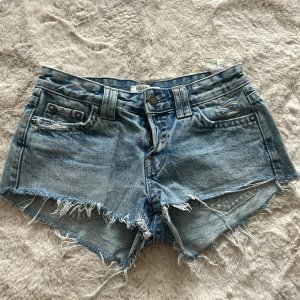 Blå Lågmidjade jeansshorts  - Snygga ljusblå lågmidjade jeansshorts från Pull&Bear med fransig, rå kant och slitna detaljer. Klassisk femficksmodell med bälteshällor och knappstängning. Perfekta för sommaren och ger en avslappnad vibe.🩷🍀