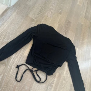 Svart tie back topp. - Svart långärmad topp med rund halsringning och tie back i ryggen. Mjukt, tunnt, skönt och väldigt stretchigt material, perfekt till jeans eller kjol. Enkel och stilren design som funkar året runt. Köpte den för flera år sen men den passar fortfarande, så himla söt och fin!!😍Säljer då den tyvärr inte används längre💗Finns ett litet hål som går superlätt att fixa annars är den i fint skick.