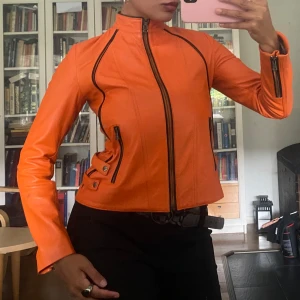 Orange skinnjacka med svarta detaljer - Säljer en riktigt snygg orange skinnjacka med svarta dragkedjor och coola detaljer vid sidorna. Perfekt statement-plagg för dig som vill sticka ut. 😍💥Strl 38 men passar absolut 34-36 också! 