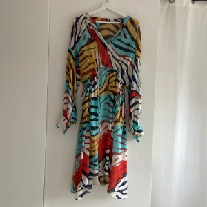 Färgglad kortklänning Soaked in Luxury - Säljer en superfin knä lång klänning från Soaked in Luxury med färgstarkt zebramönster i turkos, röd, beige, vit och svart. Klänningen har en innerklönning, v-ringning, långa vida ärmar med knapp vid manschetten och dragsko i midjan. Perfekt för dig som gillar statement-plagg!