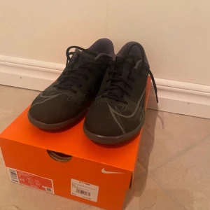 Svarta Nike fotbollsskor med snörning - Säljer ett par svarta Nike fotbollsskor med snygga grå detaljer och klassisk snörning. Skorna har en låg profil och är tillverkade i syntetmaterial för bästa känsla på planen. Perfekta för dig som vill ha stilrena och sportiga skor till fotbollsträningen.