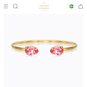 Guldarmband med rosa stenar Svedbom - Stilrent armband i guldton från Caroline Svedbom med två droppformade rosa kristaller i varje ände. Tunn och elegant design som ger en lyxig känsla och passar perfekt för att lyfta din outfit.