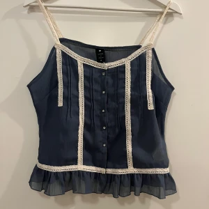 Blå linnetopp från Soaked in Luxury - Säljer en söt blå linnetopp från Soaked in Luxury med spetsdetaljer och knappar framtill. Toppen har smala axelband och en volangkant nedtill. 