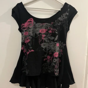 Svart topp med mönster från Sense Girlswear - Snygg svart topp från Sense med blommönster. Toppen har korta ärmar och en lätt utsvängd nederdel som ger en fin siluett.