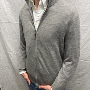 Grå kofta från H&M - Säljer en stilren grå kofta från H&M i merinoullsblandning. Koftan har en dragkedja framtill och ribbade muddar vid ärmslut och nederkant. Perfekt för lager-på-lager under kyligare dagar. Plagget sitter normalt för sin storlek. Modell på bild är 182 cm/68 kg. Hör gärna av dig vid fler frågor. Mvh, CAVI