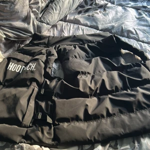 Svart pufferjacka från Hoodrich - Säljer en svart pufferjacka från Hoodrich med dragkedja och justerbara remmar på sidorna. Jackan har en hög krage och är perfekt för kyligare dagar. Den är stilren och enkel att matcha med olika outfits. Storlek S, sällan använd. Perfekt för våren nu.. pris kan även diskuteras 