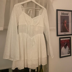 Vit klänning från Nalina - Säljer en söt vit klänning från Nalina med broderade detaljer och knytning i ryggen. Klänningen har långa ärmar och en v-ringad design. Perfekt till studenten eller konfirmation! Den är M men ganska liten i storleken så passar S