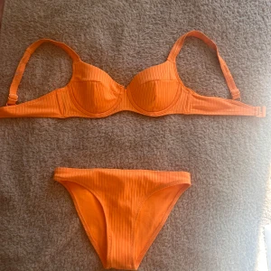Orange ribbad bikini - Snygg orange bikini med ribbad textur. Överdelen har justerbara axelband och bygel för extra stöd. Perfekt för soliga dagar på stranden eller vid poolen. Underdelen har en klassisk passform.