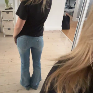 Blå bootcut jeans - Snygga blå bootcut jeans med klassisk femficksdesign och knappgylf. Perfekta för en avslappnad stil med en touch av retro. Mått: 38 cm & 83 cm
