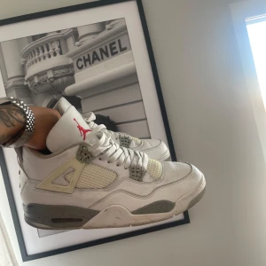  Nike Air Jordans 4 oreo  - Säljer ett par klassiska vita Nike Air Jordans med grå och röda detaljer. Skorna har snörning och en ikonisk design med Jordan-loggan på plösen och hälen. 