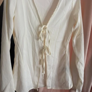Vit långärmad blus med knyt - Elegant vit blus med långa ärmar och knytning framtill. Perfekt för en stilren look.