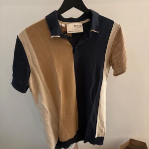 Flerfärgad pikétröja från Selected Homme - Snygg flerfärgad pikétröja från Selected Homme i beige, blå och vit. Tröjan har korta ärmar och en klassisk krage med knappar. Perfekt för en stilren och avslappnad look.