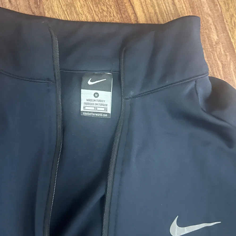Säljer ett träningsset från Nike med dragkedja och vita detaljer. Setet består av en jacka och byxor, båda med Nike-logga. Perfekt för träning eller avslappnad stil. Jackan har dragkedjor på fickorna för säker förvaring.. Puvut & Bleiserit.