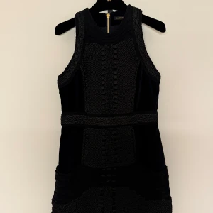 Svart klänning från Balmain x H&M - Snygg svart klänning från Balmain x H&M med unika flätade detaljer och dragkedja bak. Klänningen är ärmlös och har en elegant design som passar perfekt för speciella tillfällen och fickor i sidan.
