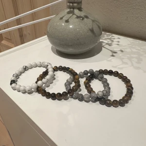 Stilrena armband i olika stenar - Säljer ett set av fyra stilrena armband med pärlor i olika stenar. Armbanden har en mix av vita, grå och bruna nyanser, vilket ger en naturlig och jordnära känsla. Perfekt för att komplettera din outfit med en touch av elegans.