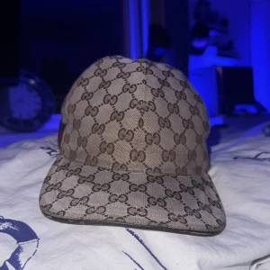 Beige keps gucci keps - Snygg beige keps från Gucci med det ikoniska monogrammönstret. Kepsen har en klassisk design med en justerbar rem baktill i grönt och rött. Perfekt för att ge din outfit en lyxig touch. Äkta såklart men kvitto finns inte.
