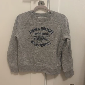 Grå sweatshirt från Zadig & Voltaire - Snygg grå sweatshirt från Zadig & Voltaire med tryck framtill. Tröjan har rund hals och långa ärmar, perfekt för en avslappnad stil. Passar perfekt till våren och ett par snygga jeans! Säljer pg av att ja köpt tröjan på Sellpy men den är för liten💗 Skriv för mer bilder, kan diskutera kring priset 