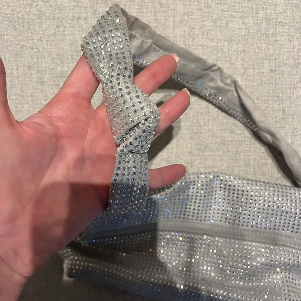 Snygg grå axelväska med glittriga detaljer från Gina tricot. Väskan har en praktisk magnetknäppning och ett innerfack med dragkedja för extra säkerhet. Perfekt för att ge din outfit lite extra bling!. Laukut & Käsilaukut.