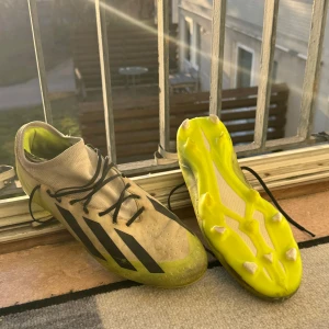Adidas Crazyfast Pro  - Snygga fotbollsskor från Adidas i vit och neongul färg med svarta detaljer. Skorna har snörning och en modern design med dobbar för bra grepp på planen. Perfekta för fotbollsträning och matcher. Skick 8/10 Strlk 44 2/3